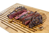 Sliced grilled steak with garlic on a slotted bamboo carving board