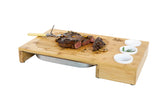 Bamboo carving board with steak, carving fork, and ceramic condiment bowls
