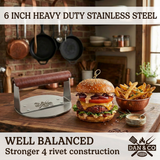 Heavy duty stainless steel burger press with wooden handle next to burger and fries on kitchen counter.