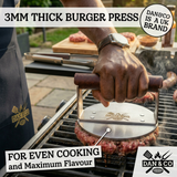 Hand using stainless steel burger press with wooden handle on grilling burger patties outdoors