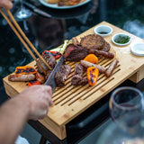 Bamboo carving board with grilled meat, sausages, vegetables and dipping bowls