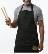 Man wearing a black kitchen apron holding bamboo tongs, logo on apron pocket