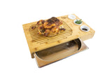 Bamboo carving board with roasted chicken, spice dishes, and drip tray on white background
