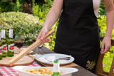 Person in black apron setting outdoor table with bamboo serving tray, drinks, and plates
