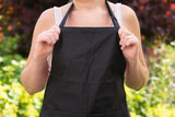 Person wearing a black kitchen apron outdoors, holding the apron straps