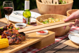 Hand using large bamboo tongs to serve grilled chicken on bamboo serving board outdoors