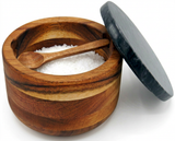 Wooden salt cellar with black lid, filled with coarse salt and a small wooden spoon
