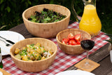 Three bamboo wooden salad bowls with salad servers on picnic table outdoors