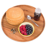 Round acacia wooden serving tray with pancakes, berries, seeds, syrup and spoon on white background.